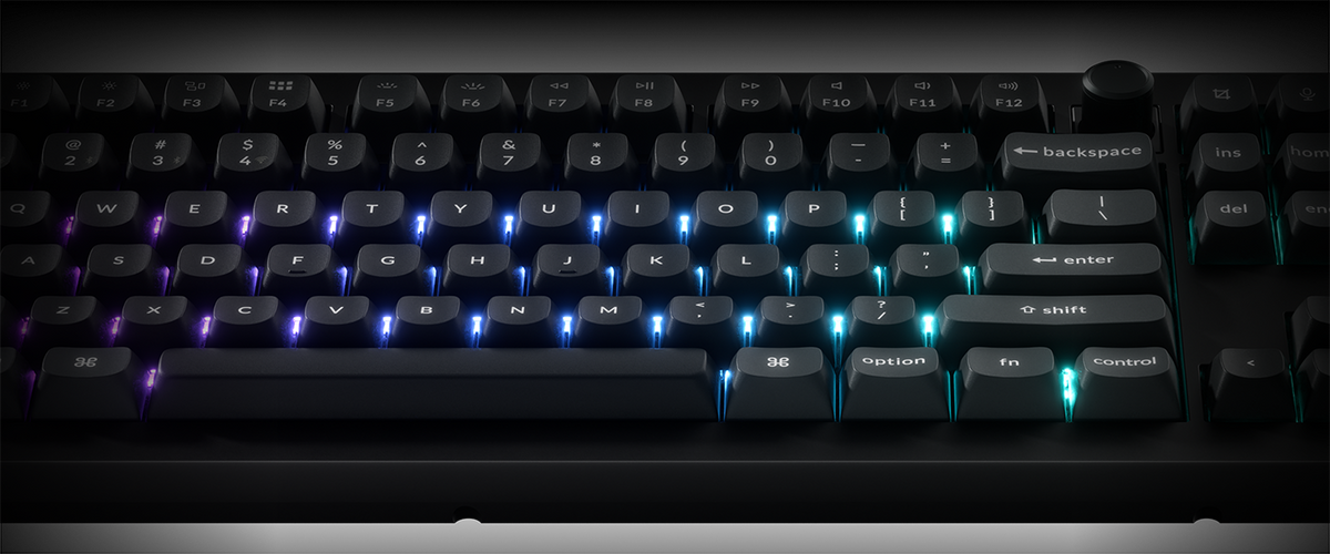 A close-up of a black mechanical keyboard with glowing RGB backlighting in shades of blue, purple, and cyan, set against a dark background.